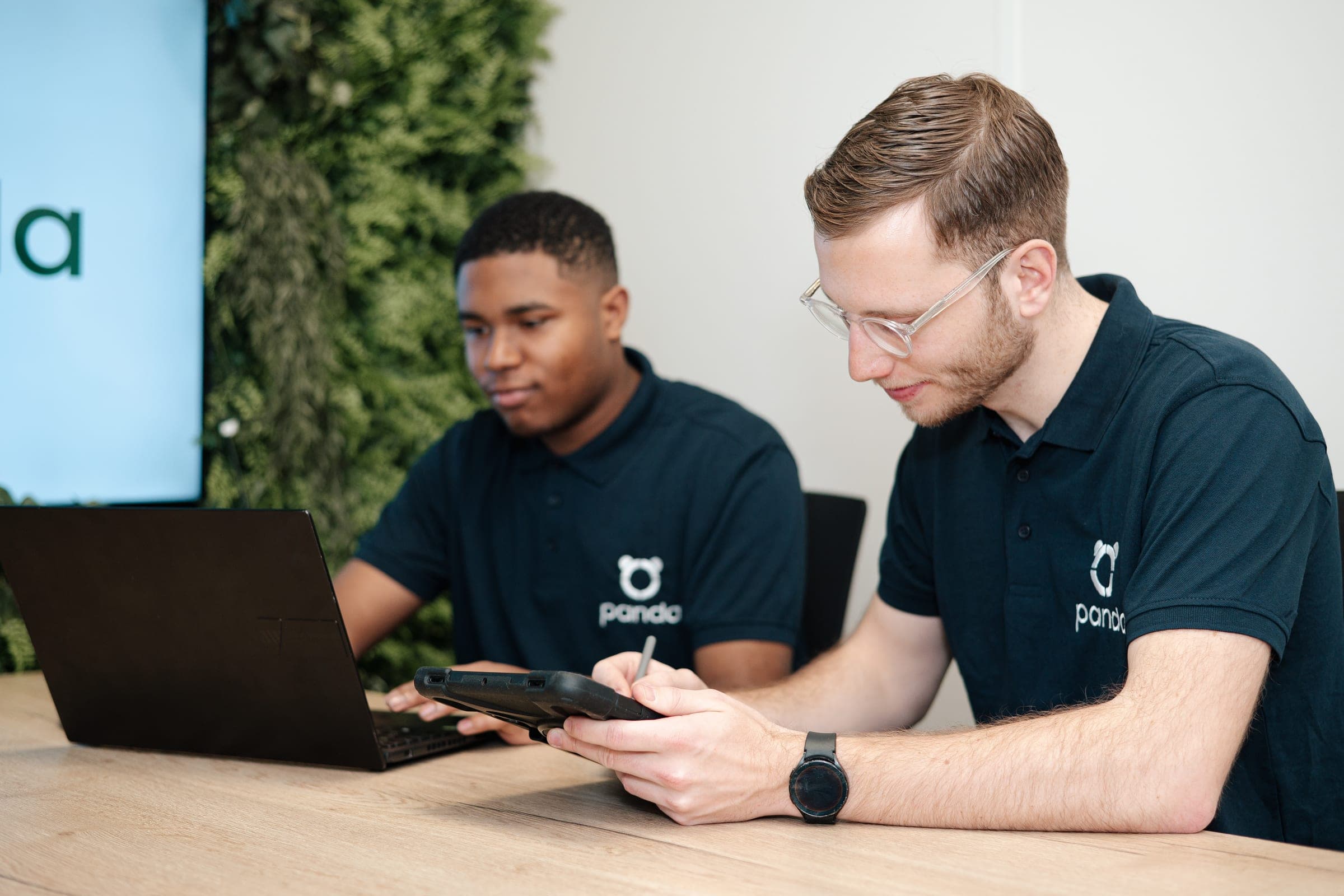 Twee Panda-medewerkers werken samen aan een houten tafel — een typisch werkmoment in onze portefeuille-trajecten